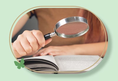 foto em detalhe de uma mulher segurando uma lupa, pesquisando nas páginas de um livro